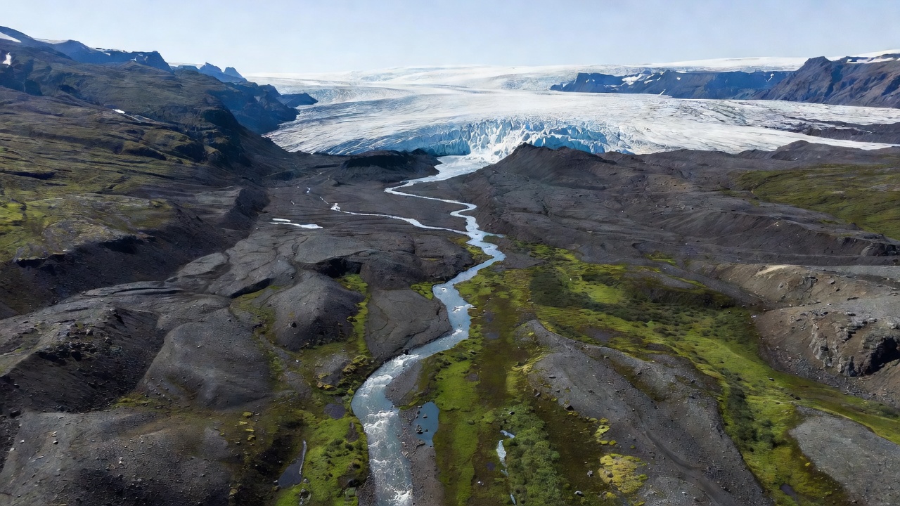 Vista aérea de un valle sin hielo con un arroyo de deshielo y manchas de vegetación verde junto al agua